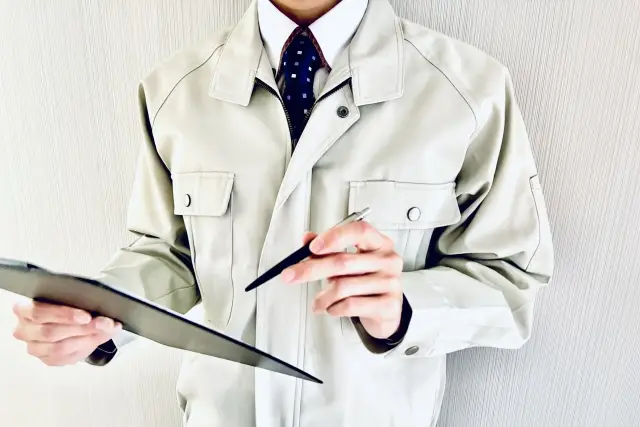 バインダーを持つ作業着の男性